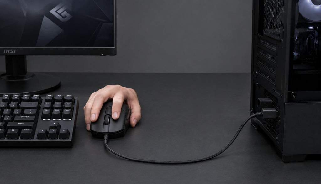 Wired gaming mouse with USB cable connected to PC on dark desk
